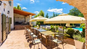 An outdoor dining area with tables and chairs, umbrellas, and a pool in the background. - Villa Damiana in Domijani i (Zminj)