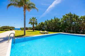 A clear blue swimming pool with a palm tree and lounge chairs on the side. - Villa Pelagos Blue in Rhodes (Rhodes)