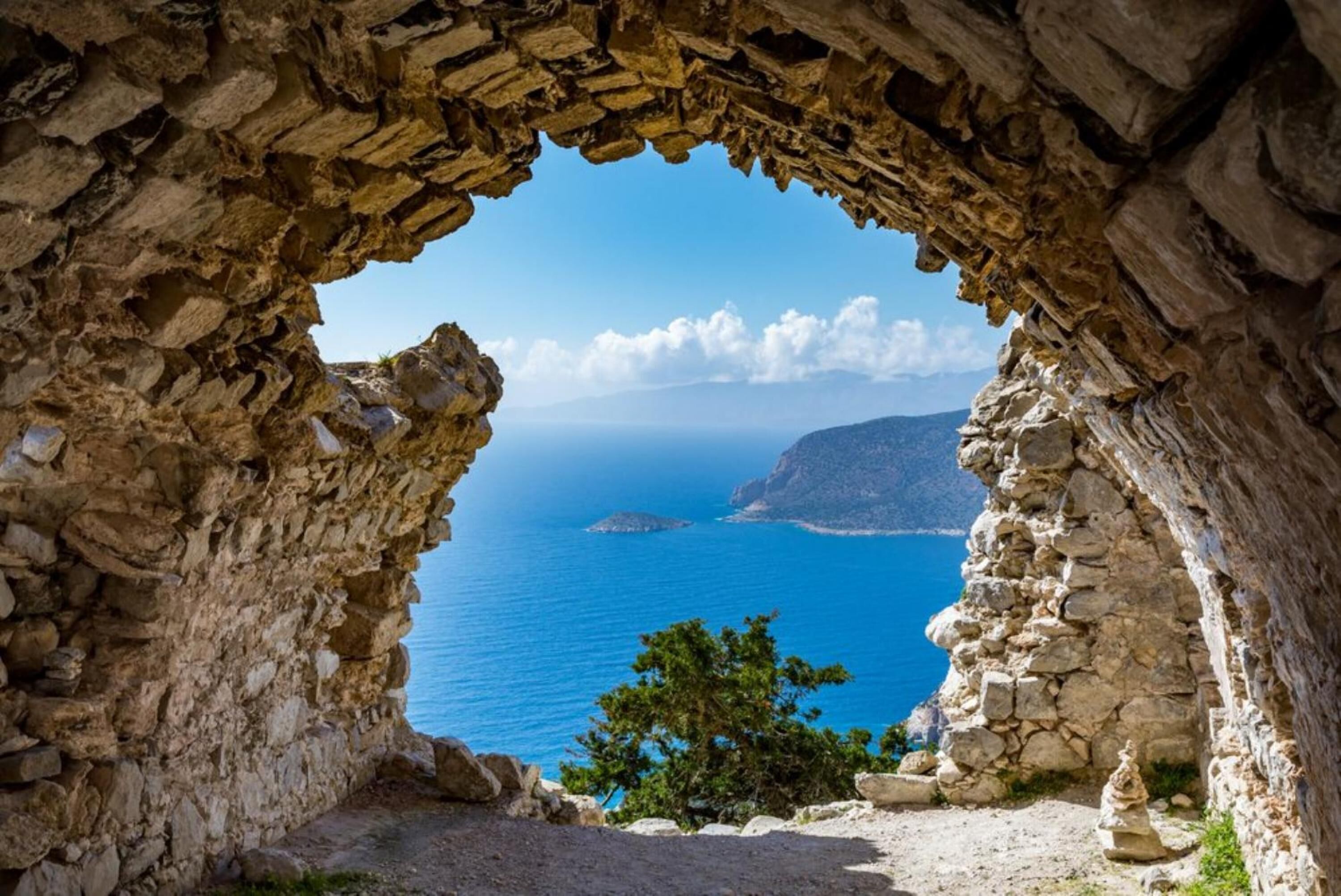 Ein Steinbogen, der zu Blick auf das Meer und eine entfernte Insel führt.