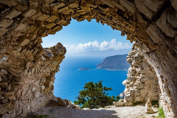 Ein Steinbogen, der zu Blick auf das Meer und eine entfernte Insel führt.