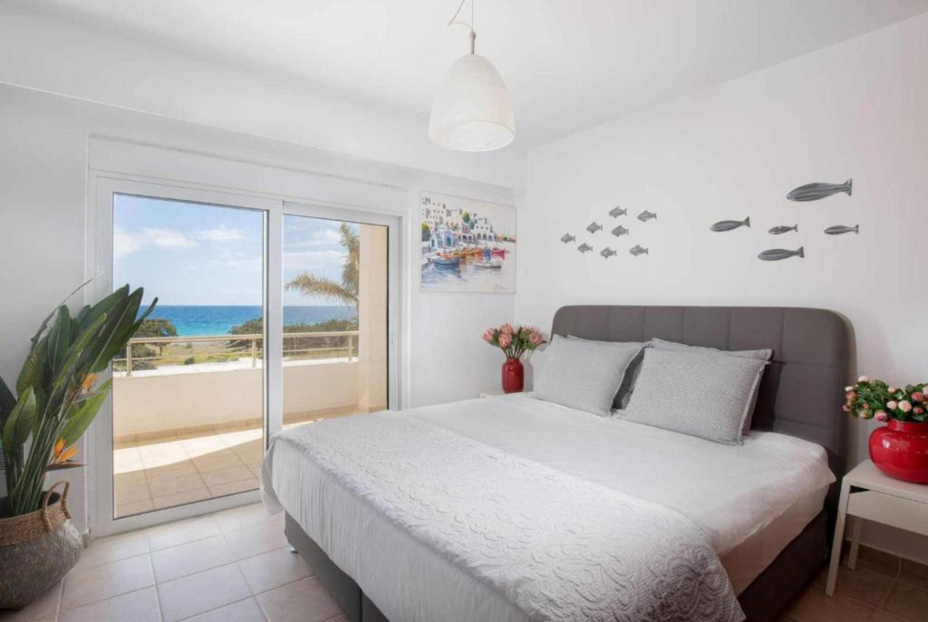 A bedroom with a large bed, a view of the sea through a sliding door, a ceiling light, and a wall with fish decals.