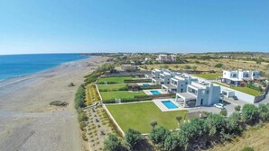 Et kystnært boligområde med moderne huse, en swimmingpool og en strand i baggrunden.