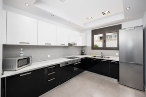 A modern kitchen with black and white cabinetry, a stainless steel refrigerator, a microwave, and a window providing a view of the outside.