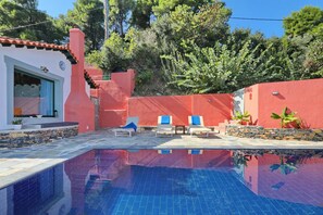 En swimmingpool med liggestole, en stenvæg og en bygning med rød facade.
