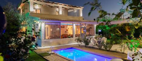 A two-story house with a swimming pool, outdoor seating, and a well-lit garden.