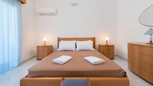A neatly arranged bedroom with a bed, two bedside tables, a dresser, and an air conditioning unit on the wall.