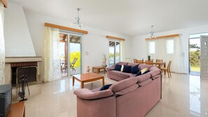 A spacious living room with a fireplace, a pink sofa, a dining area, and large windows.