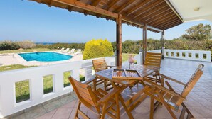 A covered outdoor area with a pool, wooden furniture, and a view of the sea.