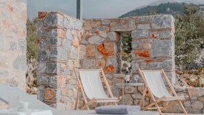 A stone wall with two wooden lounge chairs and a table. - Villa Dioni Ena in Ditiki Mani (West Mani)