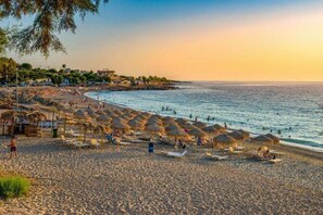 Une plage avec des parasols, des chaises longues et des gens.