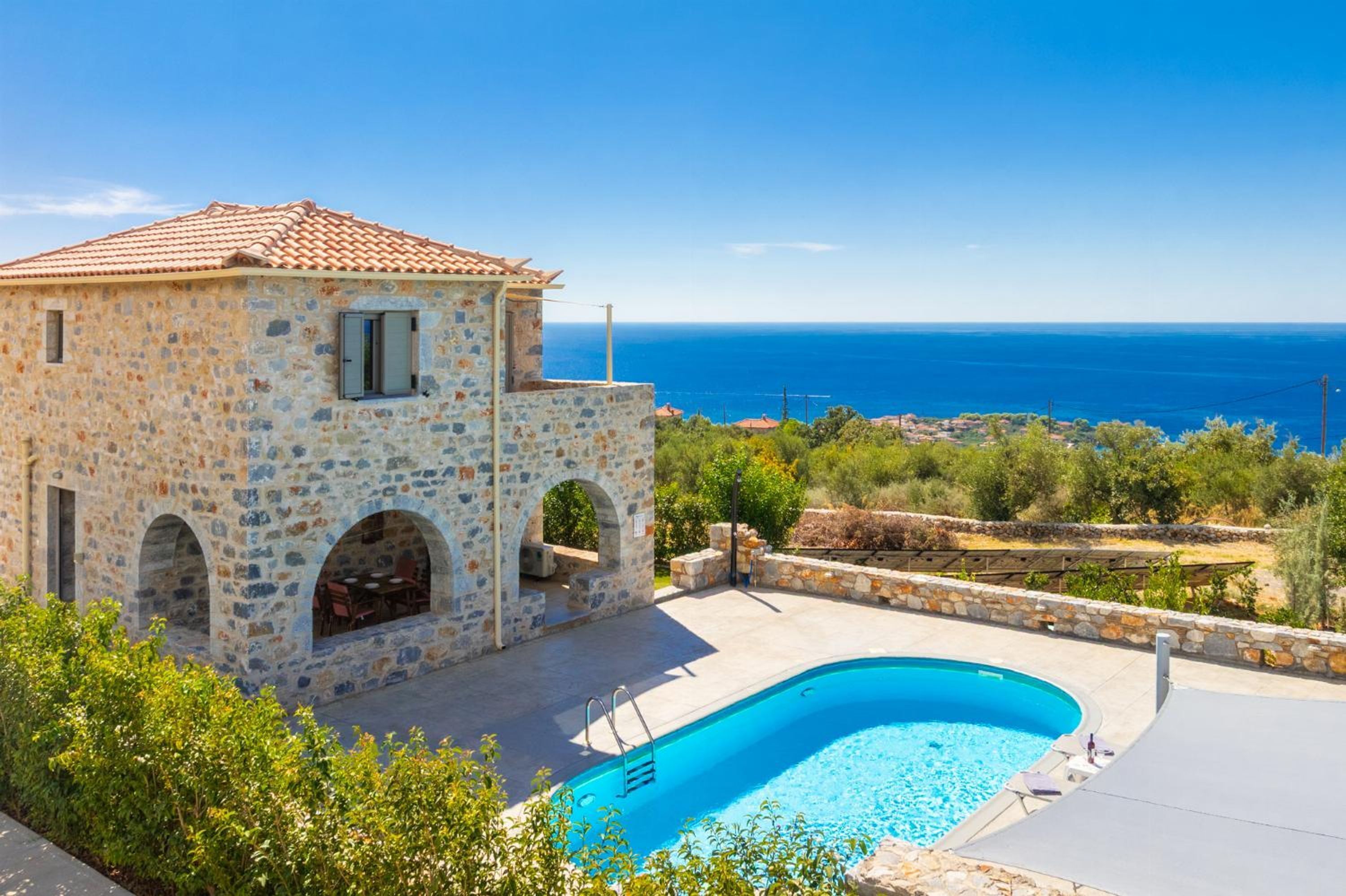 A stone building with a swimming pool, arched windows, and a view of the sea.