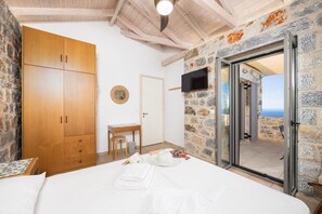 Une chambre à coucher comprenant un lit, une armoire en bois, des murs en pierre, un téléviseur et une porte donnant sur un balcon avec vue.