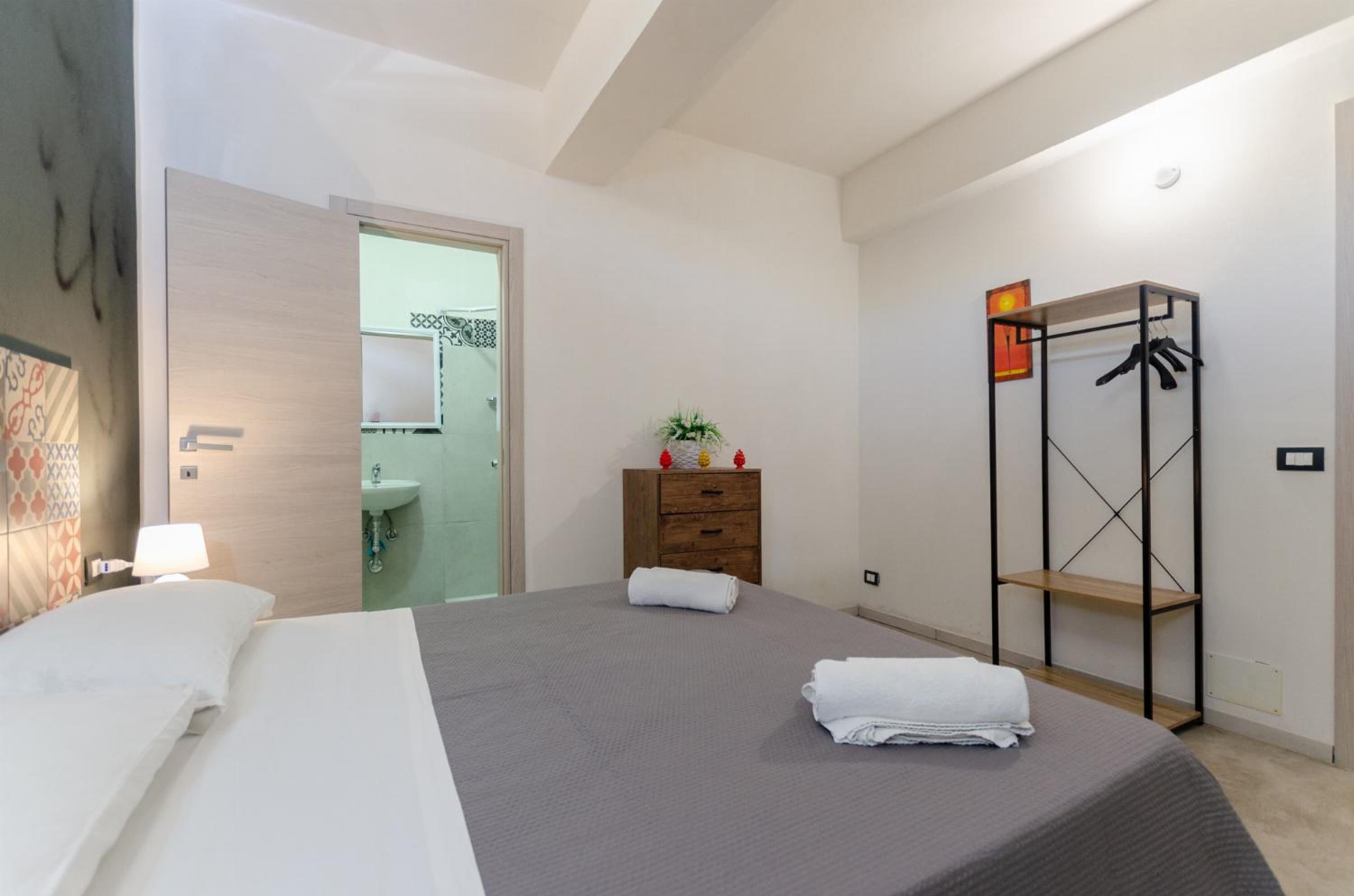 A hotel room with a large bed, a wooden dresser, a small plant, and a metal rack for hanging clothes.