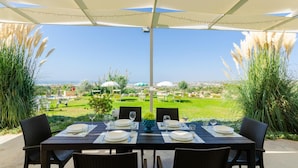 An outdoor dining area with a view of the sea, surrounded by greenery and umbrellas. - Villa Padima in Scicli (Scicli)