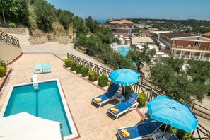 Área de piscina no terraço com espreguiçadeiras e guarda-sóis, cercada por um muro de pedra e vegetação.