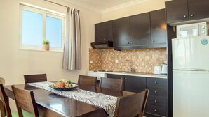 Et lille køkken med mørke skabe, et flisebeklædt backsplash, et hvidt køleskab og et spisebord med stole.