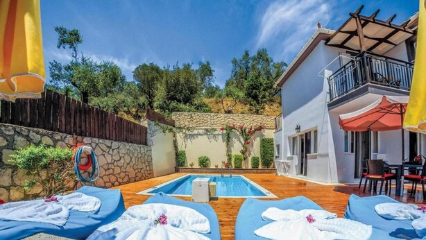 A poolside area with lounge chairs, a stone wall, and a building with a balcony. - Villa Dimi in Tsilivi (Zakynthos)