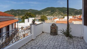 Une terrasse sur le toit, dotée d’un sol en pierre, d’une balustrade en fer forgé et offrant une vue sur une ville côtière et des collines au loin.