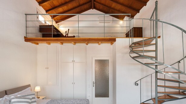 Une chambre avec un espace en mezzanine, un escalier en colimaçon et un lit agrémenté d’oreillers à rayures.