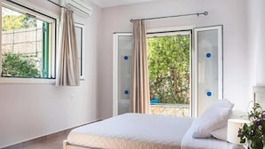 A bedroom with a bed, a window with curtains, and a view of greenery outside. - Villa Olga in Ionian Islands (Kefalonia)