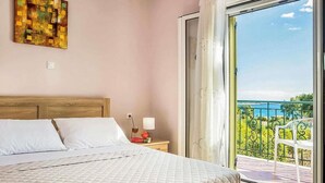 Ein Schlafzimmer mit einem Bett, einem Nachttisch, einer Lampe und Blick auf einen Balkon mit Geländer und einem Stuhl.