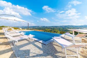 Una piscina con sillas de descanso y sombrillas, rodeada de grava y con vistas a un paisaje pintoresco.