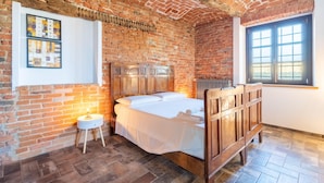 Een kamer met een bakstenen muur, een houten bed, een klein nachtkastje en een raam.