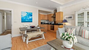 A modern living room with a grey sofa, a coffee table with a vase of flowers, and a dining area with a wooden table and chairs. - Bryn Y Mor - Tenby Apartment Sea Views (Tenby)