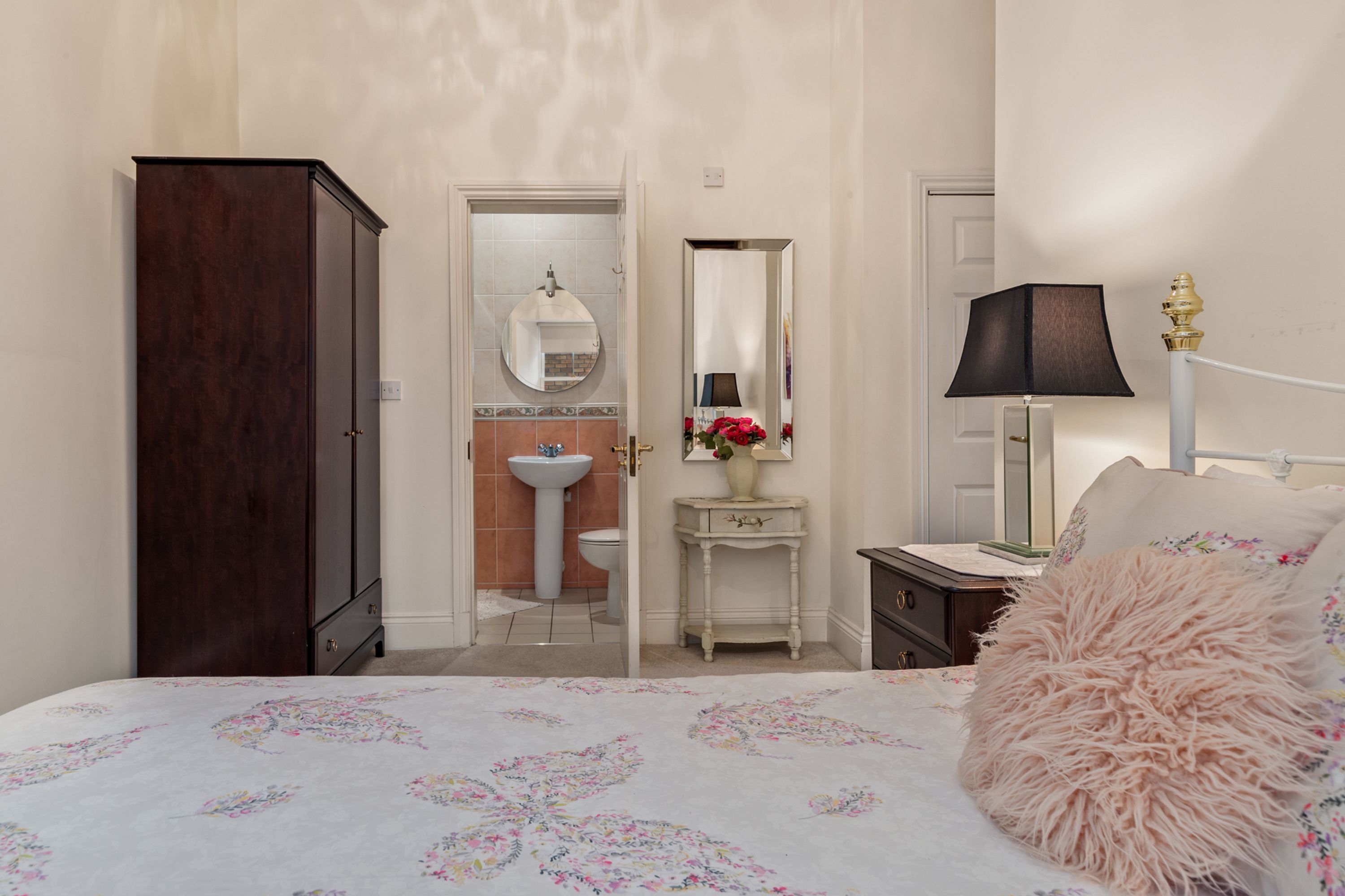 Une chambre à coucher comprenant un lit, une commode, une coiffeuse avec un miroir, une lampe et une porte donnant sur une salle de bain.