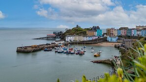 A coastal town with colorful buildings, a harbor with boats, and a lighthouse on a hill. - Bryn Y Mor - Tenby Apartment Sea Views (Tenby)