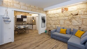Un salon moderne avec un mur en pierre, un canapé gris agrémenté de coussins jaunes et une table à manger en bois.