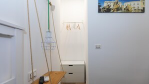 Un couloir étroit avec un banc en bois, un luminaire suspendu, une armoire blanche et un tableau accroché au mur.