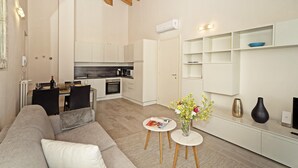 Una sala de estar moderna con un sofá, una mesa de comedor con sillas, una zona de cocina y una pequeña mesita con un jarrón.