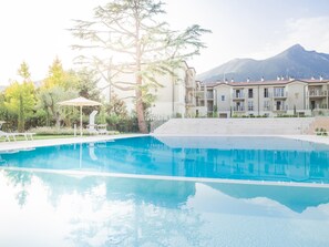 Une piscine entourée de chaises longues et de parasols, avec une végétation luxuriante et une montagne en toile de fond.