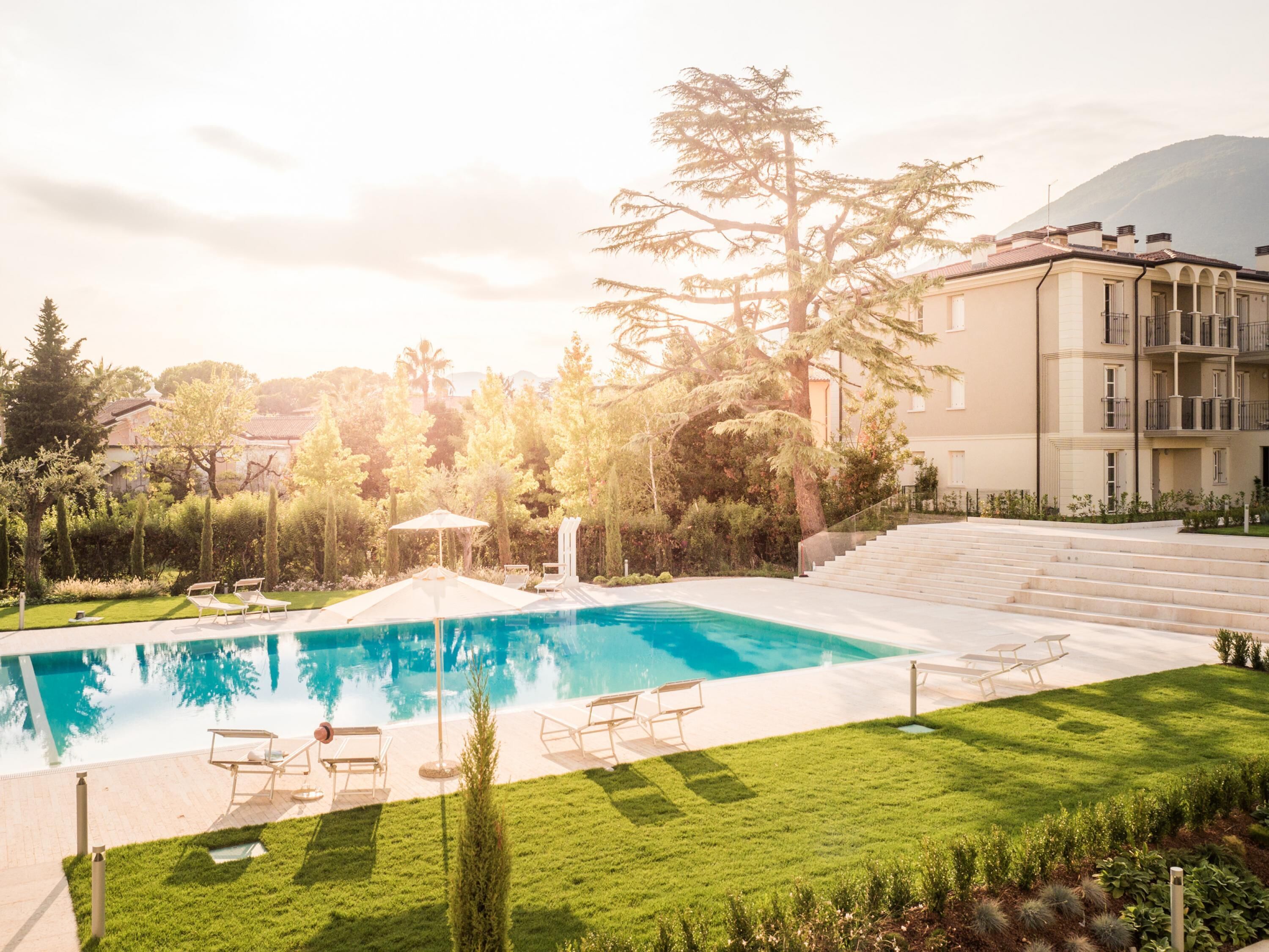 A swimming pool with lounge chairs, a well-maintained lawn, and a building with balconies.