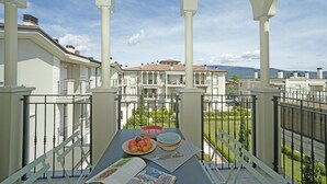Un balcón con una mesa dispuesta para comer, con vistas a una zona residencial con varios edificios y un cielo despejado.
