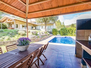 A covered patio with a pool, stone walls, and outdoor furniture.