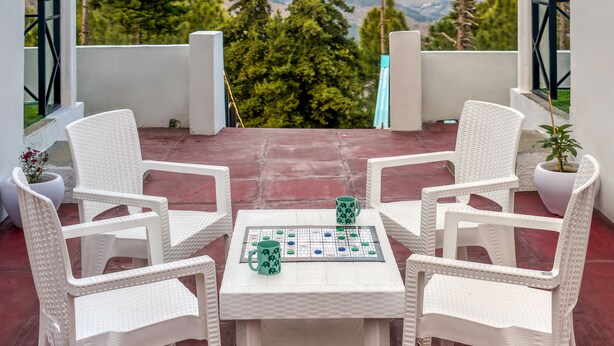 A covered patio with white wicker furniture and a table set for two, overlooking a mountainous landscape. - TRH Ekuketh (Bhikyasain)