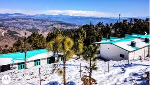 A building with a green roof, surrounded by snow-covered ground and trees, overlooking a mountainous landscape. - TRH Ekuketh (Bhikyasain)