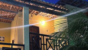 Una casa de dos pisos con un balcón, una puerta de madera y una escalera que sube al piso superior.