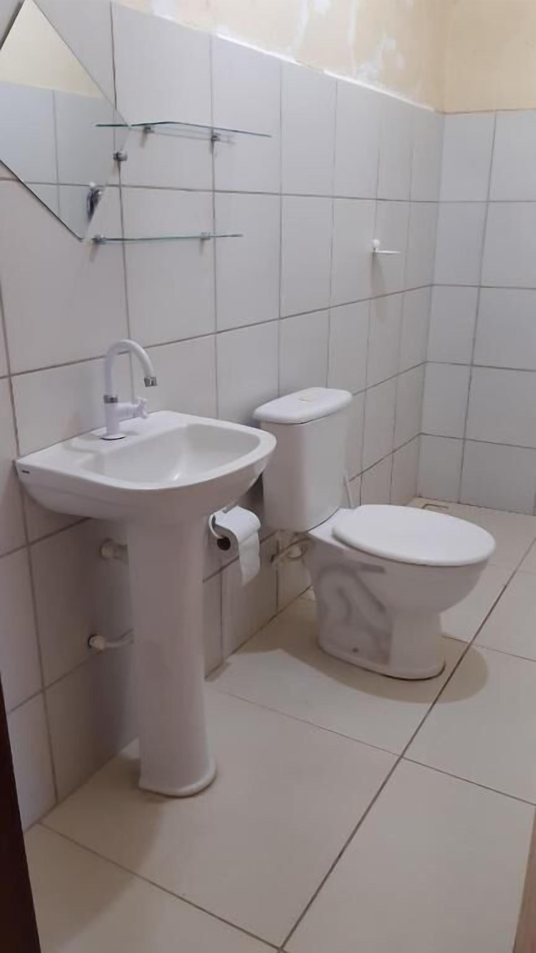 A small, clean bathroom with white tiles, a sink, and a toilet.