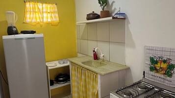 A compact kitchen with a refrigerator, stove, sink, and a yellow wall.