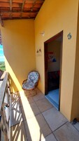 A balcony with a wicker chair, a door with a number, and a small wall decoration.
