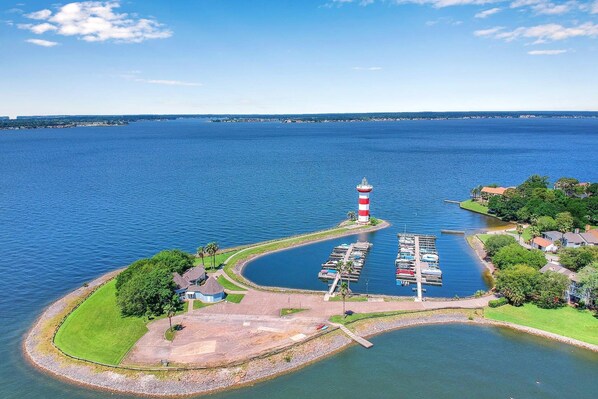 An aerial view of a marina with a lighthouse, boats, and a small island with houses. - Lake Conroe Condo | Near Ren Fest + Waterfront Dining | Peaceful Porch + Gated Community (Montgomery)