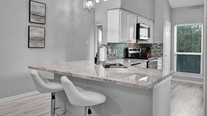 A kitchen with a marble countertop, white bar stools, and a hanging light fixture. - Lake Conroe Condo | Near Ren Fest + Waterfront Dining | Peaceful Porch + Gated Community (Montgomery)