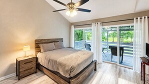 A bedroom with a bed, nightstand, lamp, ceiling fan, and a view of a balcony with outdoor furniture. - Lake Conroe Condo | Near Ren Fest + Waterfront Dining | Peaceful Porch + Gated Community (Montgomery)