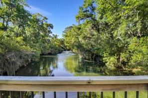 Une terrasse en bois surplombe une rivière paisible, bordée de chaque côté d’une végétation luxuriante.