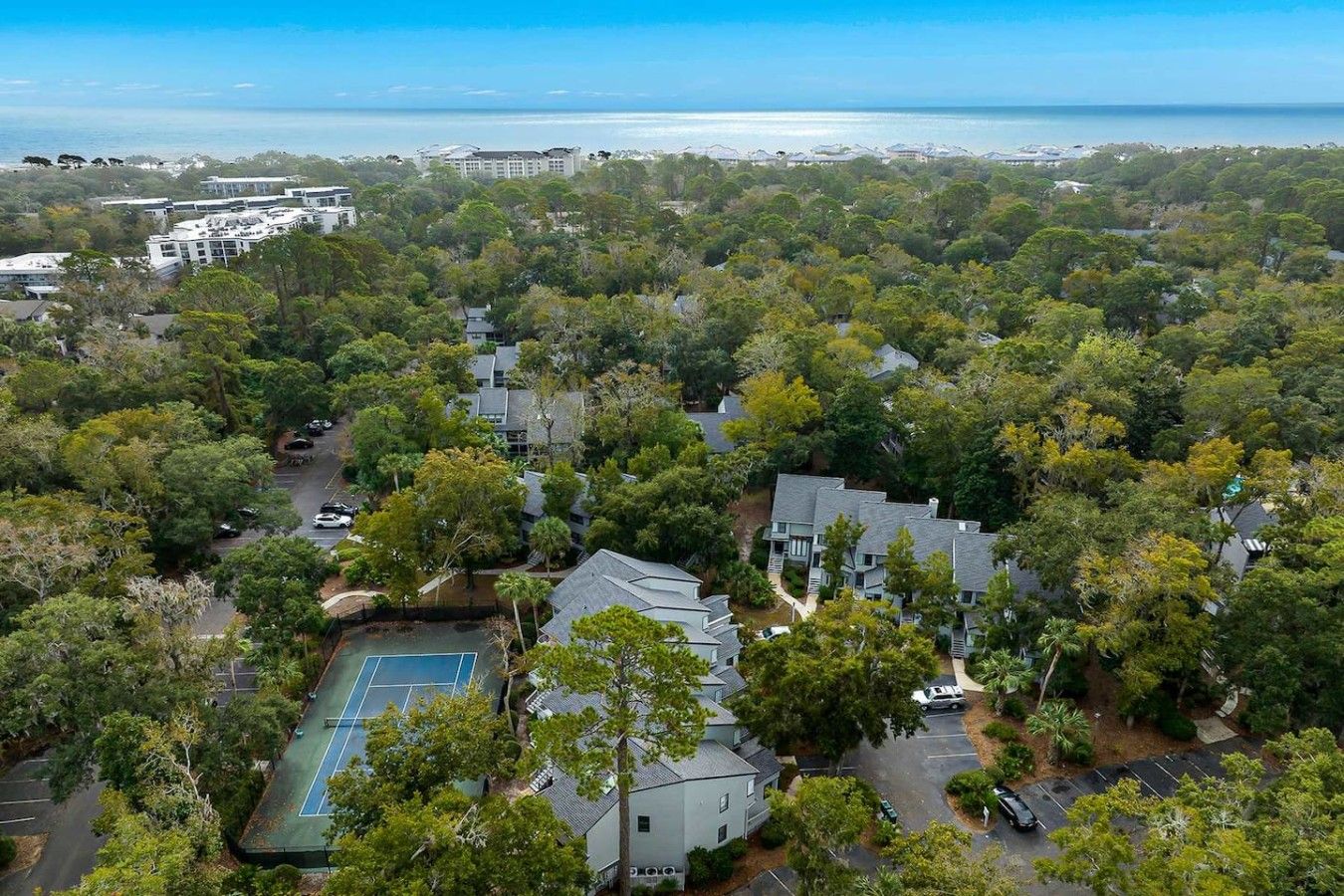 An aerial view of a residential area with houses, a tennis court, and a view of the ocean.