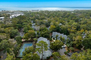 An aerial view of a residential area with houses, a tennis court, and a view of the ocean.