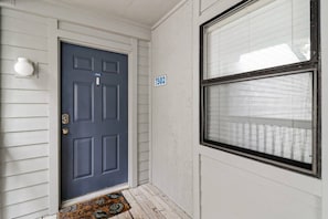 A front door with a number plate, a window with blinds, and a doormat.